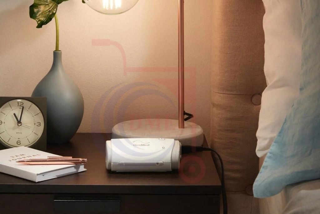 Resmed AirMini AutoSet Portable CPAP machine on bedside table next to clock and lamp