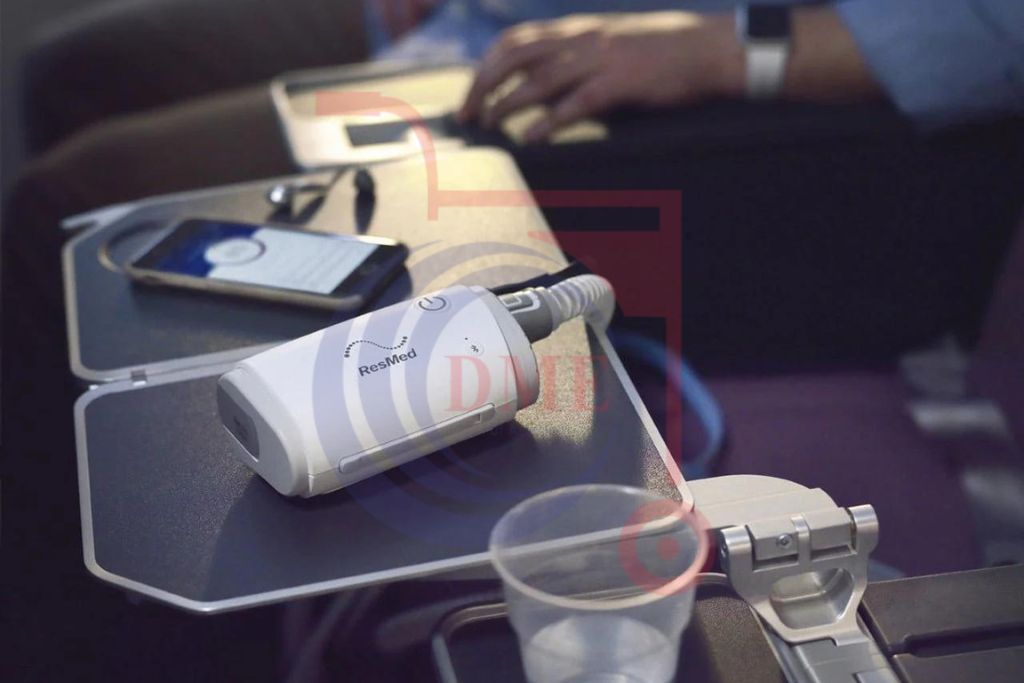 Resmed AirMini AutoSet Portable CPAP device resting on a tray table beside a smartphone and a cup