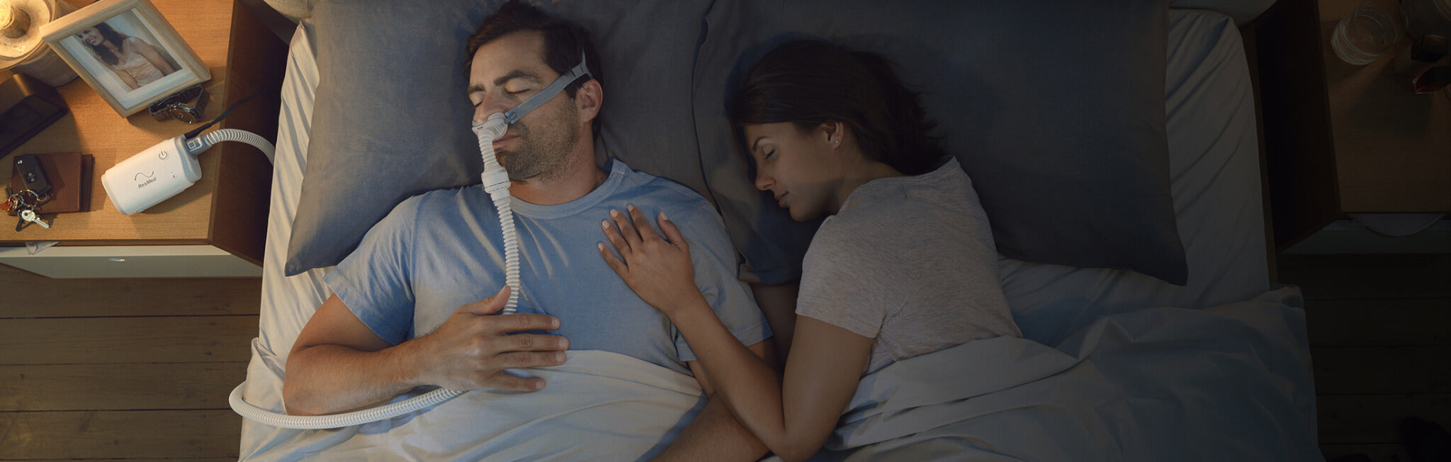 Man using Resmed AirMini AutoSet Portable CPAP machine while sleeping next to partner in bed