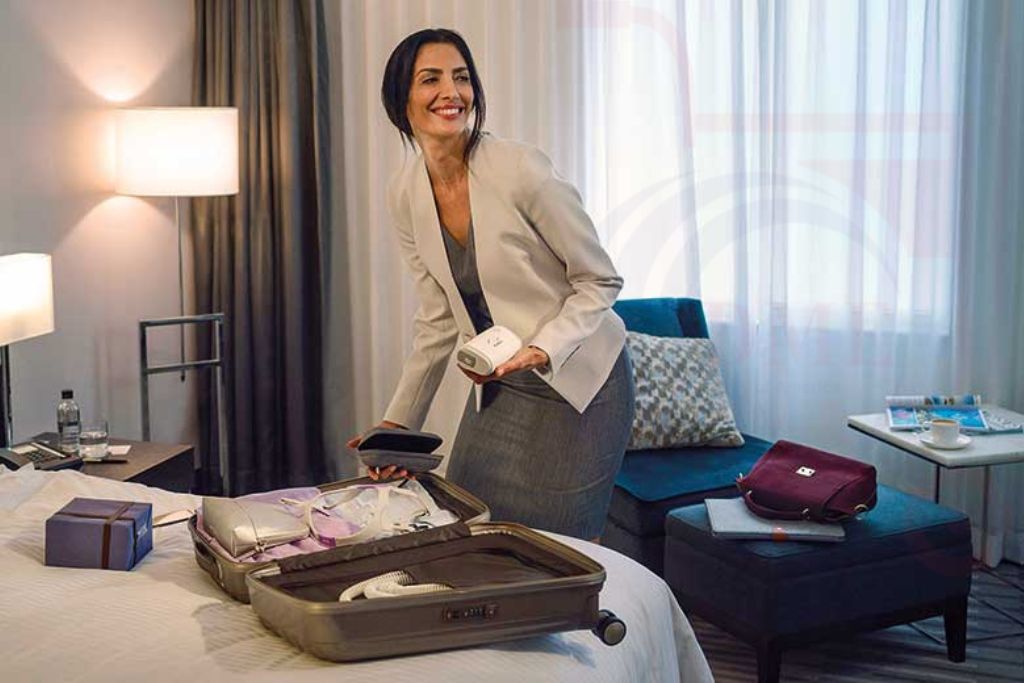 Woman packing Resmed AirMini AutoSet Portable CPAP device into suitcase in hotel room