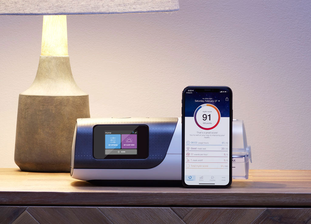 Resmed AirSense 11 CPAP machine on nightstand with smartphone displaying sleep data app